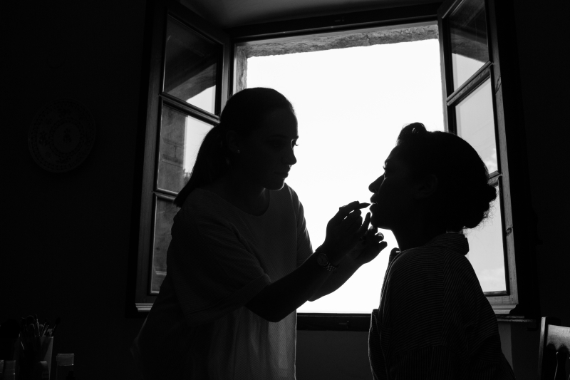Novia delante de ventana cuando la están maquillando - Fotografía de boda